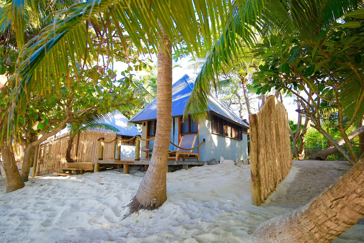 A beachside resort with a thatched-roof building, a wooden deck, and a sandy beach.