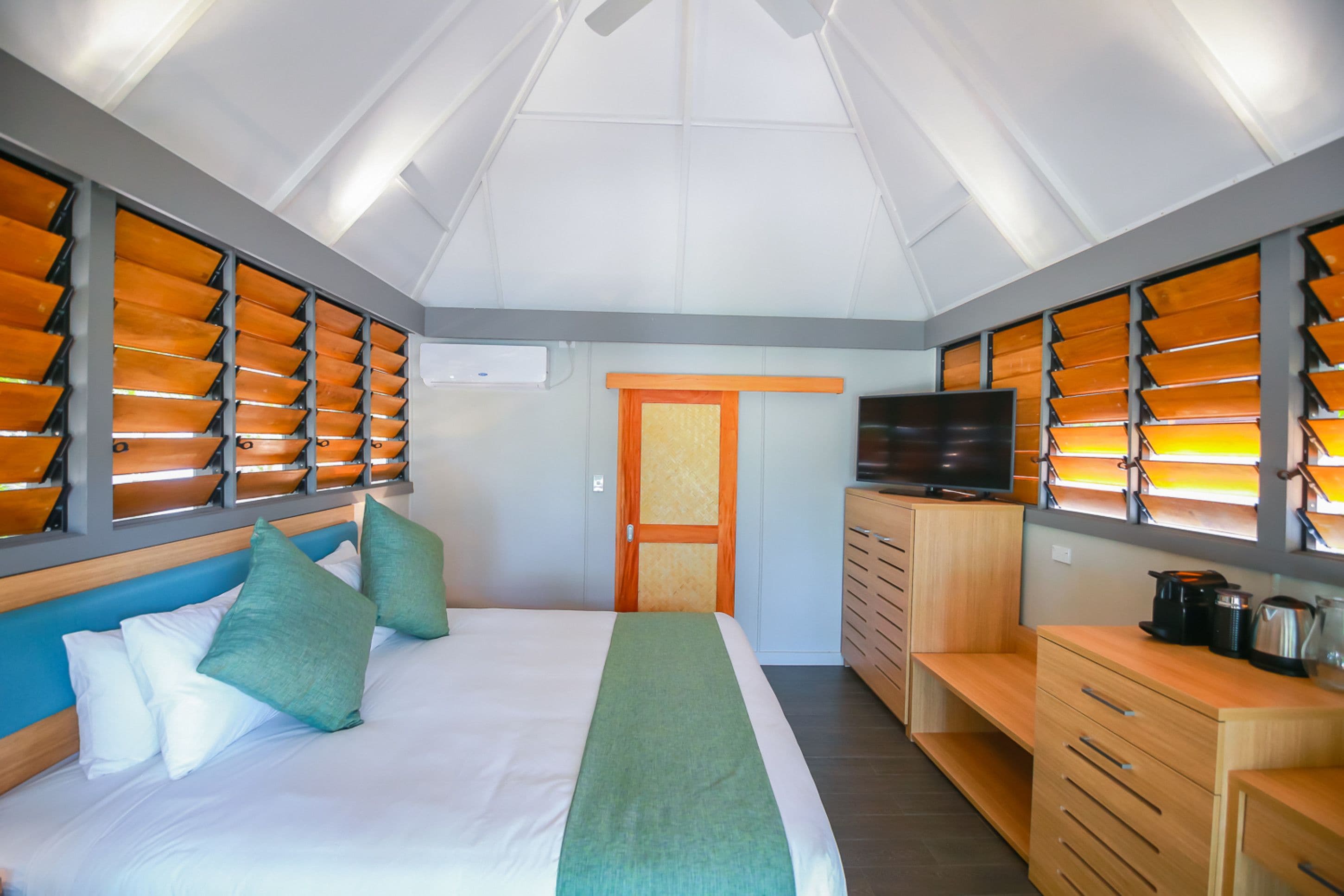 Una habitación de hotel con una cama, televisión, cómoda de madera y kitchenette.