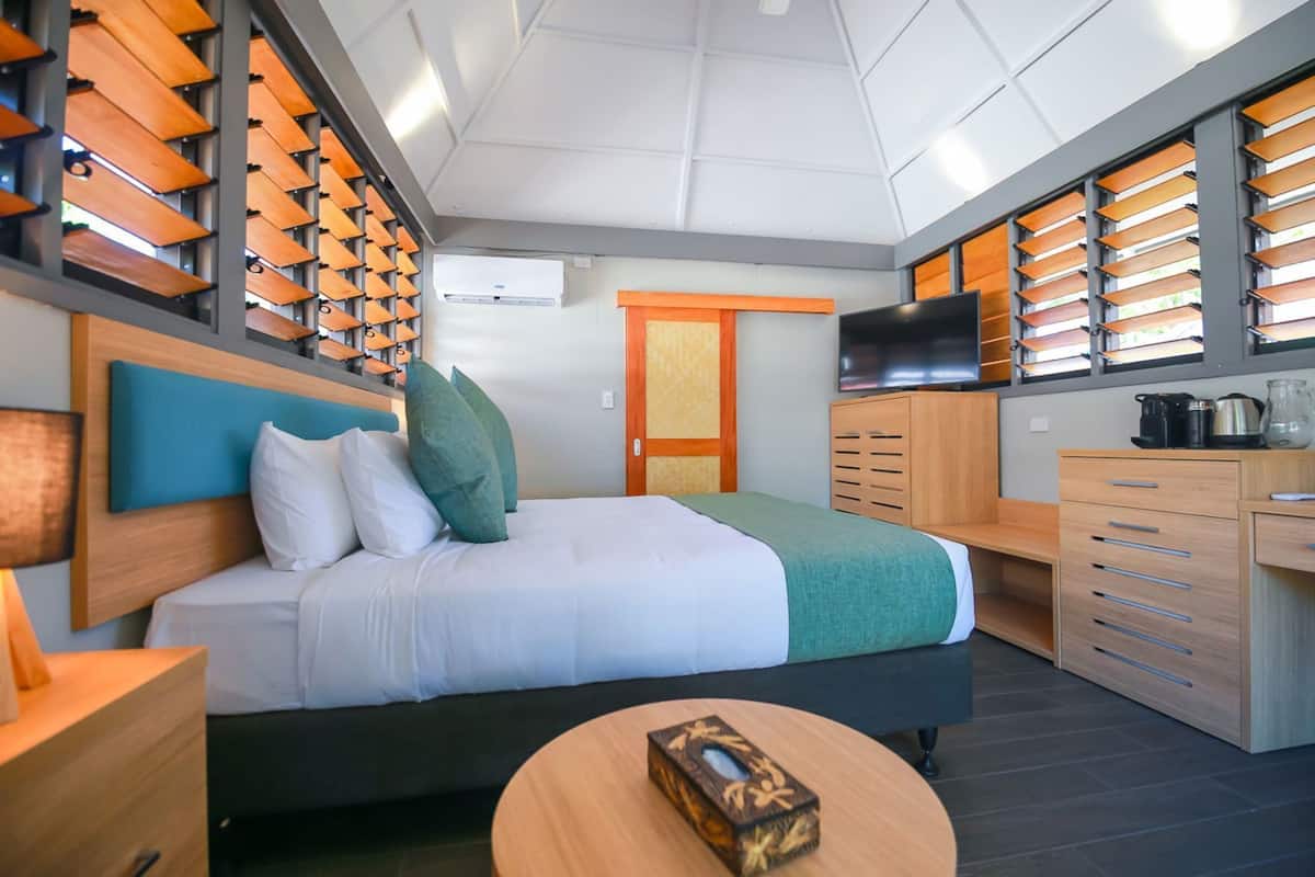 A modern hotel room with a bed, a desk, a TV, and a kitchenette.