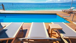 A wooden deck with a pool and lounge chairs facing a beach.