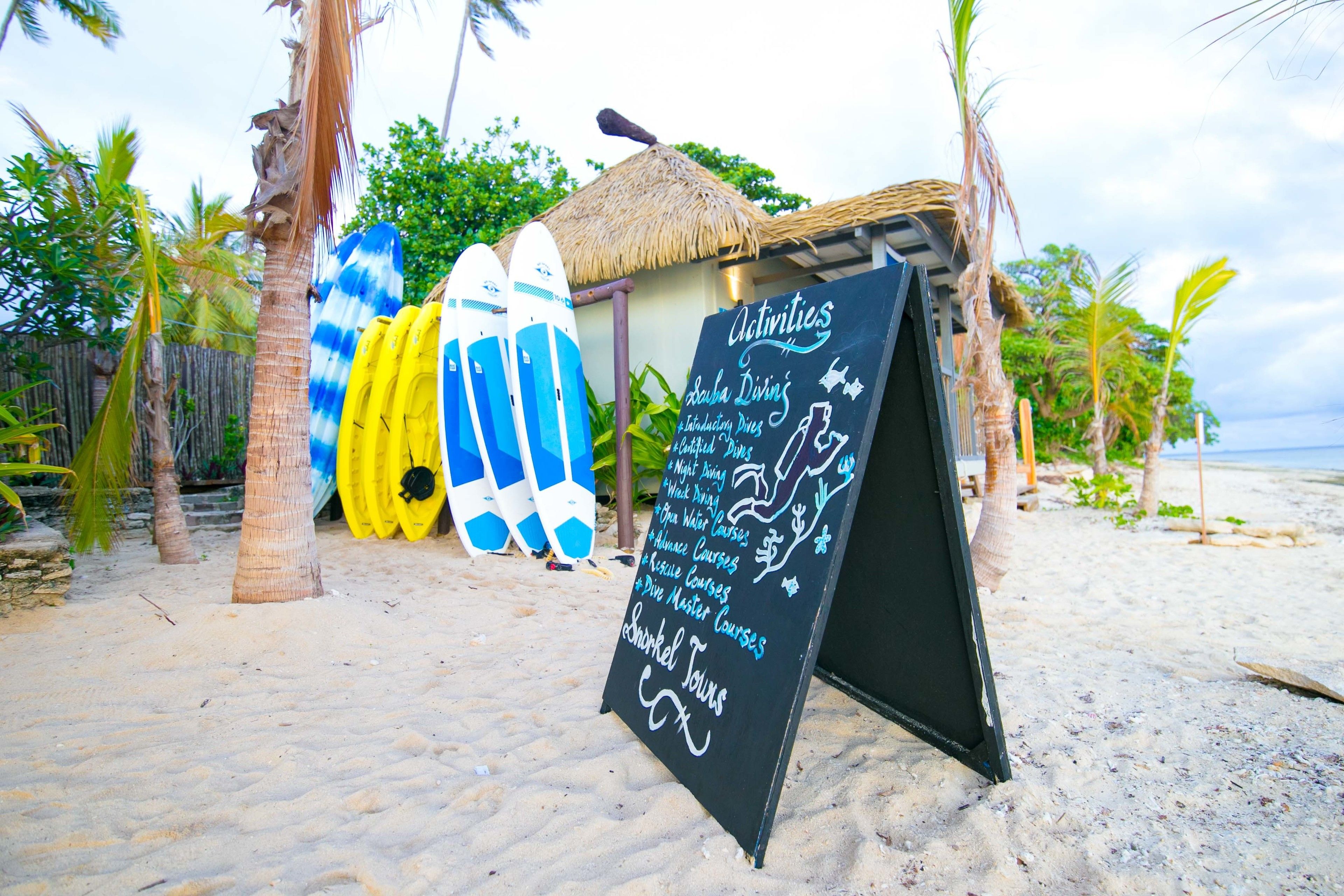A beachside location with surfboards, a thatched-roof hut, and a chalkboard listing activities like snorkeling and diving courses.