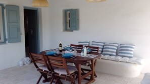 A dining area with a round wooden table, blue plates, and a bottle of wine. There are striped cushions on a white sofa and a wicker basket on the floor.