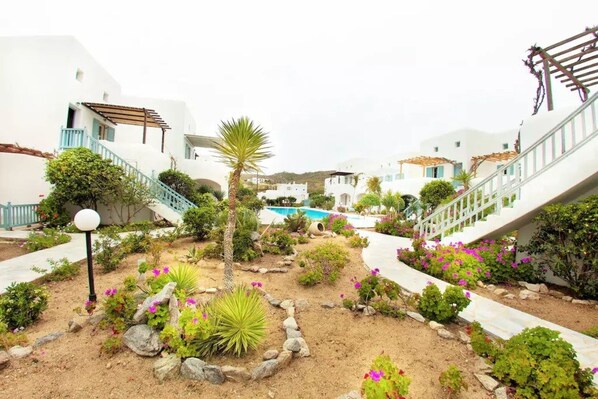A courtyard with white buildings, a swimming pool, and various plants and rocks.