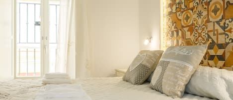 Una cama bien hecha con almohadas y toallas dobladas, una pared con estampado y una ventana con cortinas.