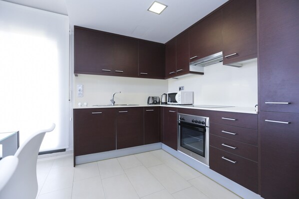 A modern kitchen with dark brown cabinets, a stainless steel oven, and a white countertop. - TROPICANA - Penthouse Sea View - Communal Pool (Cambrils)