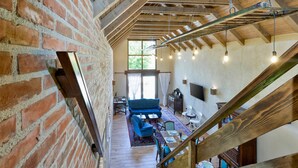 A spacious loft with exposed wooden beams, a brick wall, and a large window providing natural light.