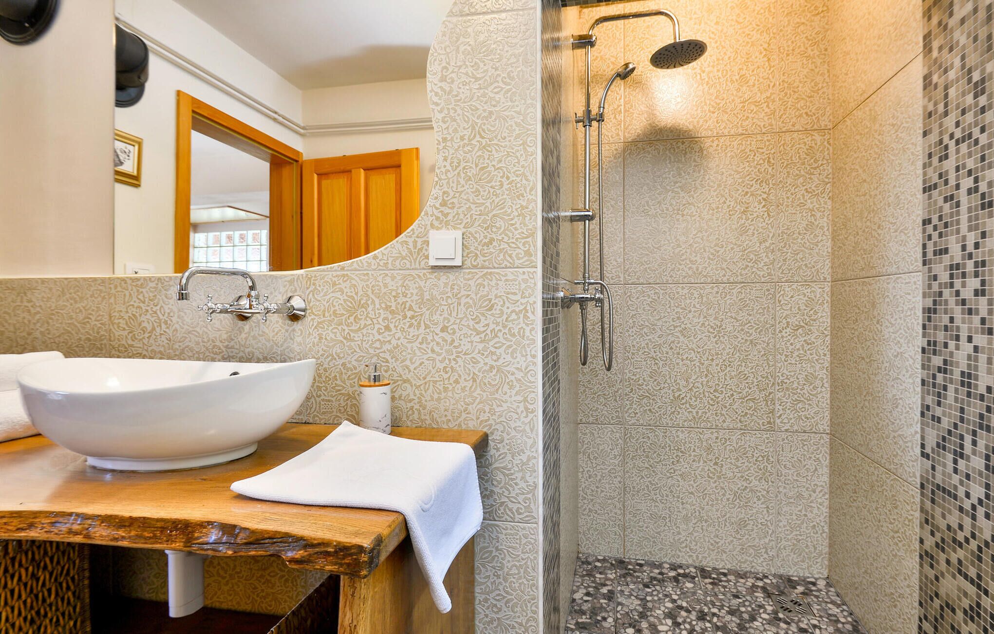 A bathroom with a large white vessel sink, a wooden vanity, a shower with a glass enclosure, and patterned tiles.