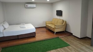 A room with a bed, a sofa, a green rug, an air conditioner, and a mounted TV. - 328 Apple Hotel Shah Alam (Shah Alam)
