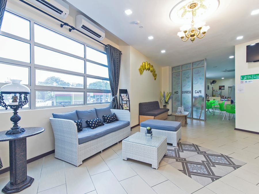 A modern hotel lobby with a sofa, a coffee table, a chandelier, and a view of the city through large windows.