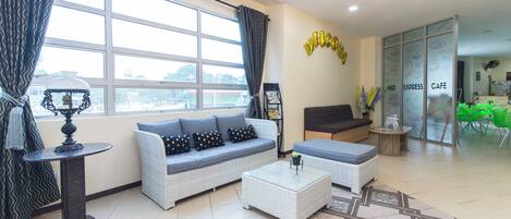 A modern hotel lobby with a sofa, coffee table, and a glass partition with 'NED EXPRESS CAFE' signage.