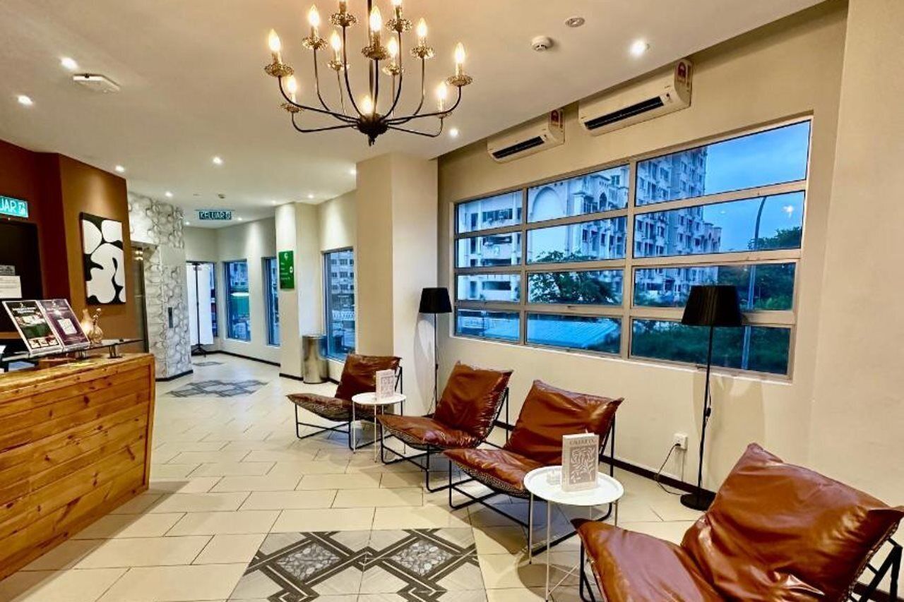 A hotel lobby with a reception desk, leather seating, a chandelier, and large windows with a view of buildings.