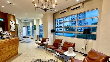 A hotel lobby with a reception desk, leather seating, a chandelier, and large windows with a view of buildings.