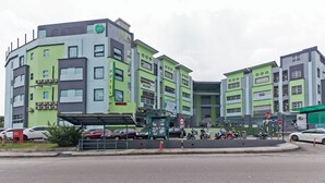 Un hôtel à plusieurs étages, doté d’une façade verte et grise, de nombreuses fenêtres et d’une enseigne bien visible indiquant la présence d’un café et d’une boulangerie.