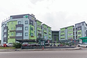 Ein mehrstöckiges Hotel mit einer grün-grauen Fassade, zahlreichen Fenstern und einem sichtbaren Schild für ein Café und eine Bäckerei.