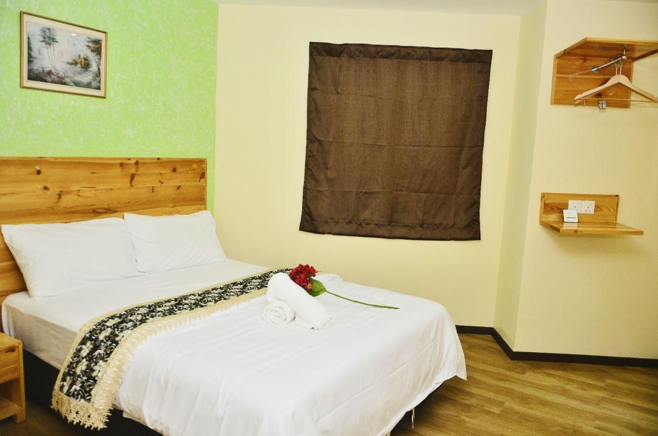 Quarto de hotel com cabeceira de madeira, uma cama grande com roupa de cama branca, cortina marrom, prateleira de madeira com cabide e uma moldura com um quadro na parede.
