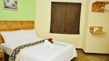 Quarto de hotel com cabeceira de madeira, uma cama grande com roupa de cama branca, cortina marrom, prateleira de madeira com cabide e uma moldura com um quadro na parede.