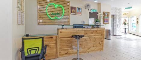 A reception desk with a wooden finish, a neon heart-shaped sign, and a reception area with a chair and a fan.