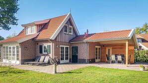 Ein zweigeschossiges Haus mit rotem Ziegeldach, Ziegelaußenwand und überdachter Terrasse mit Gartenmöbeln.