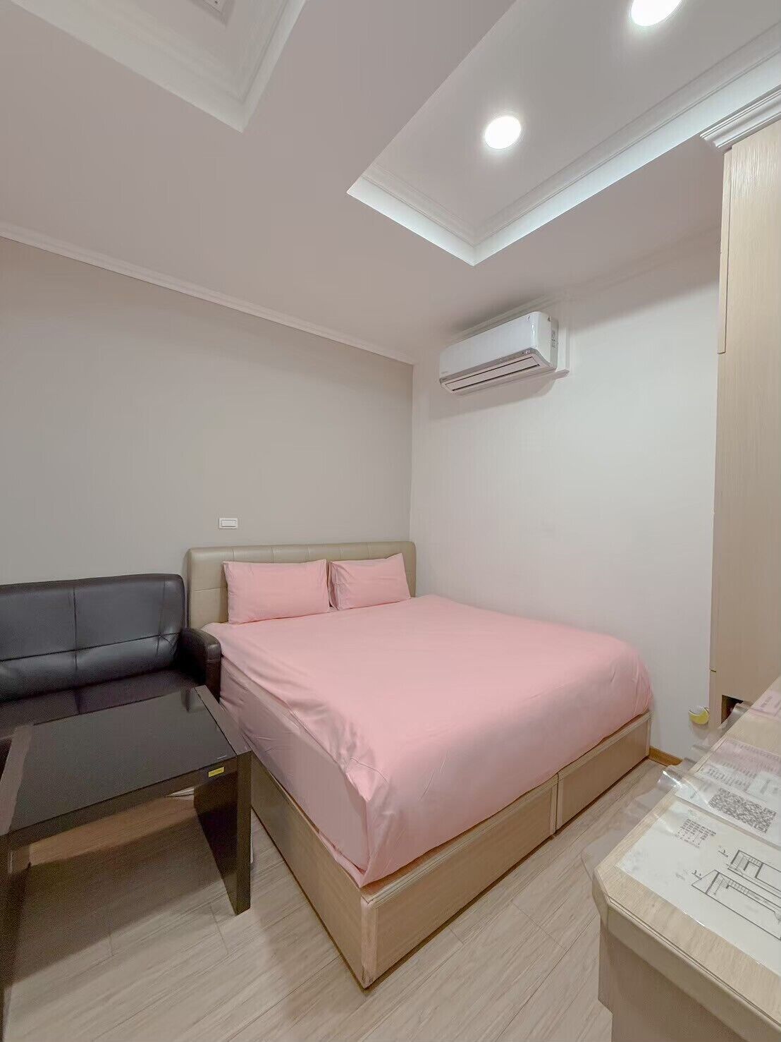 A bedroom with a bed, a desk, and an air conditioning unit.