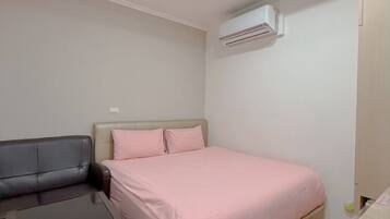 A bedroom with a bed, a desk, and an air conditioning unit.