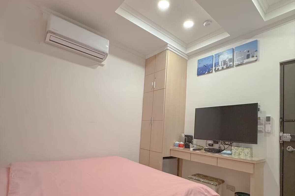 Une chambre avec un lit, un bureau avec une télévision, un climatiseur et une armoire.