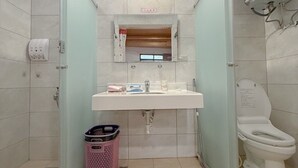 Une salle de bain compacte avec une douche à parois de verre, un lavabo blanc, des toilettes et un ventilateur de plafond.
