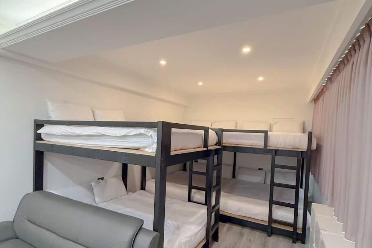 Une chambre avec un lit superposé, un canapé gris et un escalier menant à un niveau supérieur.