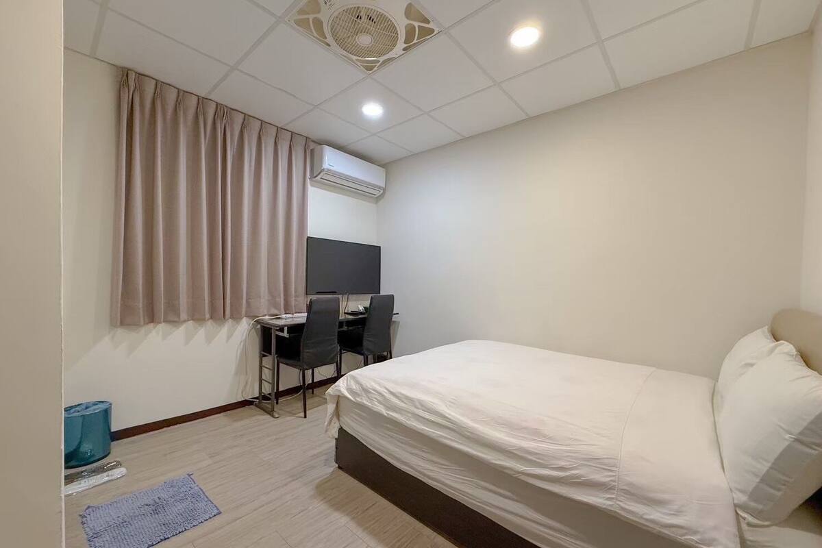 Une chambre d’hôtel équipée d’un lit, d’un bureau avec un ordinateur, d’une télévision et d’un ventilateur de plafond.