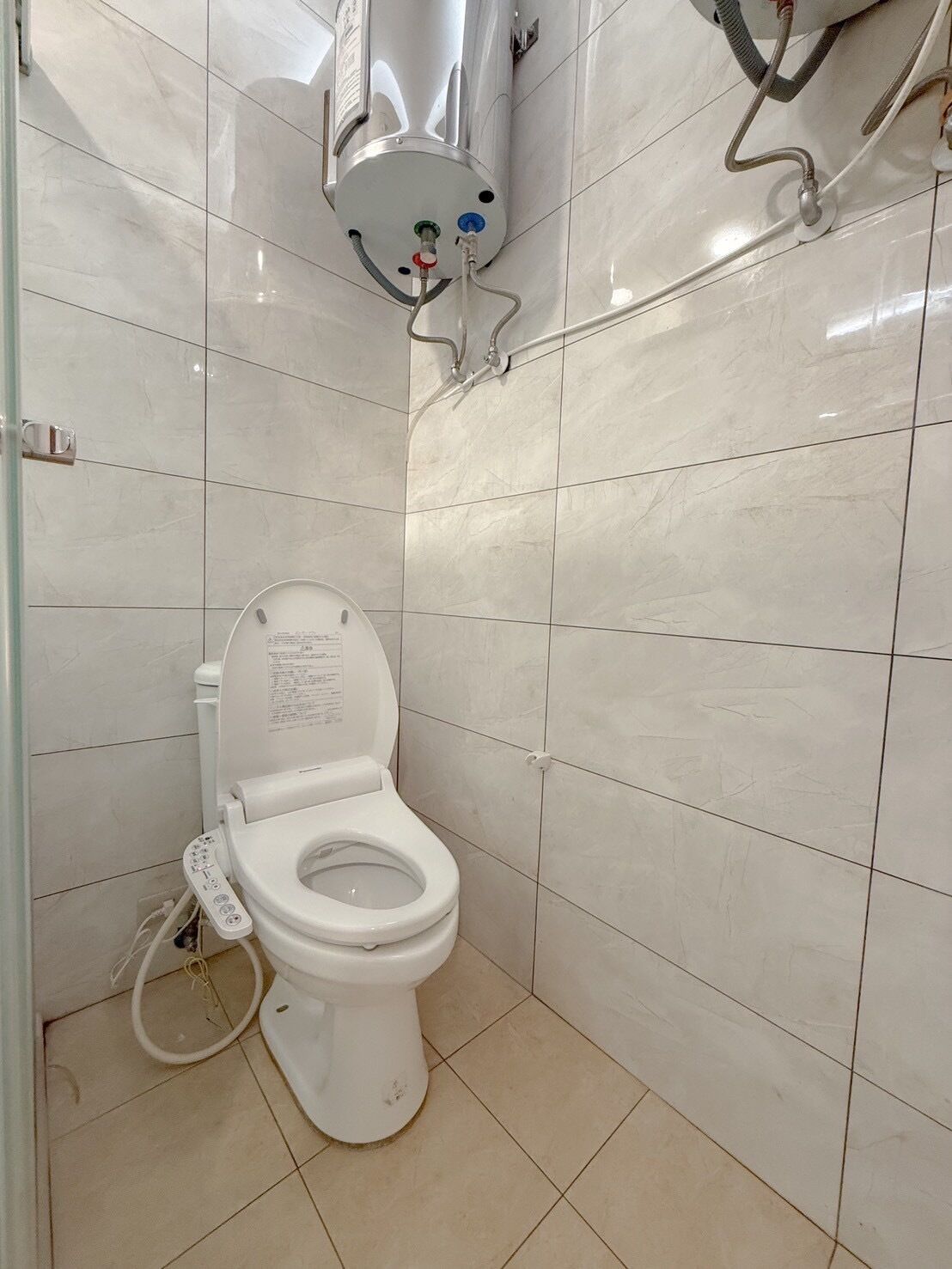 Un baño moderno con inodoro blanco, calentador de agua instalado en la pared y panel de control.