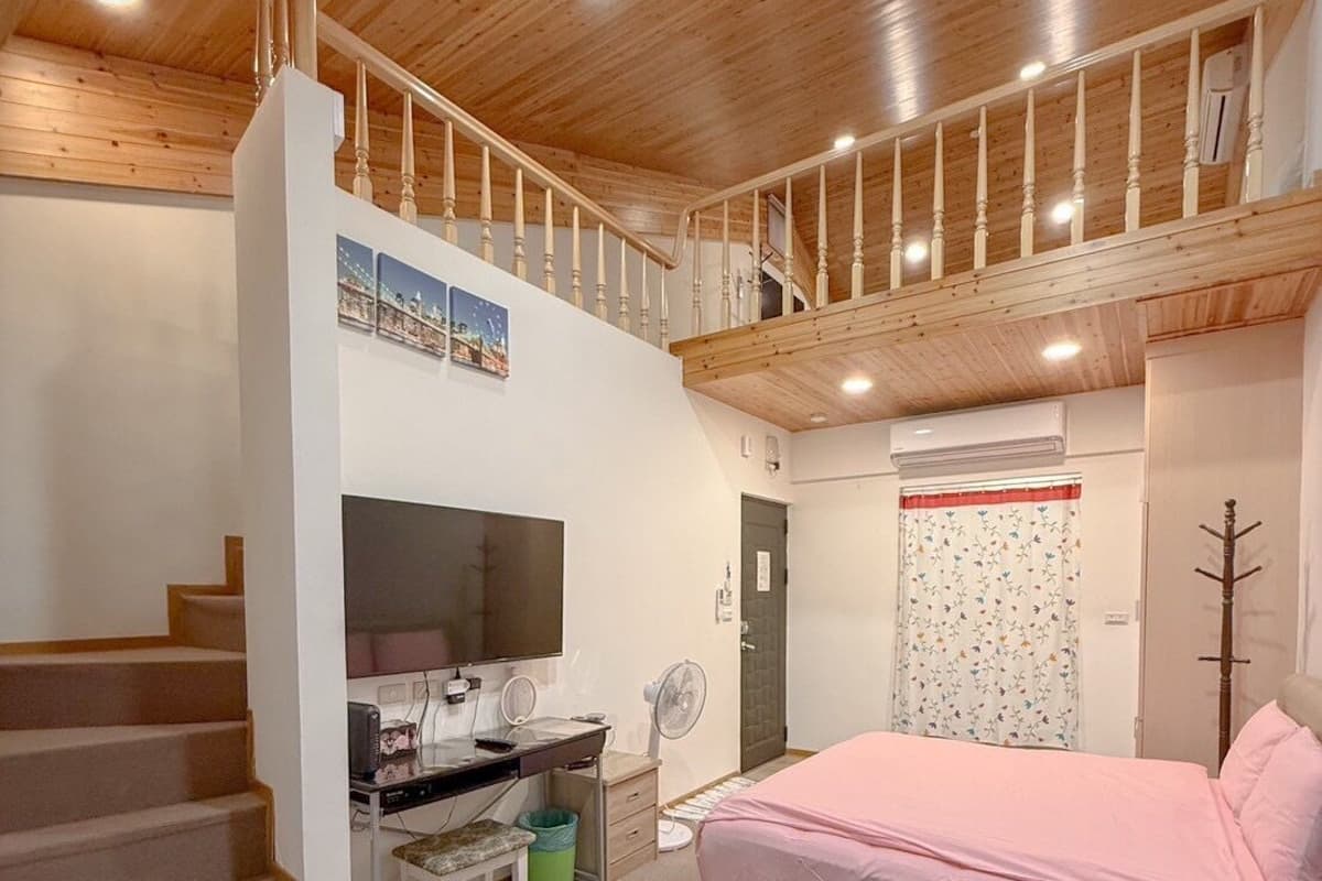 Une pièce confortable avec un escalier en bois, un lit, un bureau avec un ordinateur et une télévision.