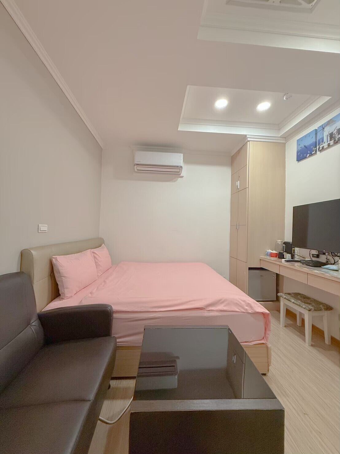 A compact room with a bed, a sofa, a desk, a television, and an air conditioning unit.