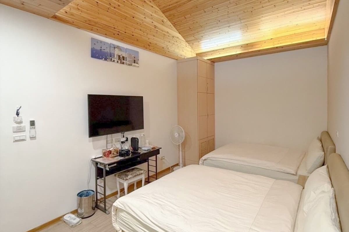 Une chambre avec un plafond en bois, un téléviseur à écran plat, un bureau avec une chaise et deux lits.