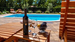 Una mesa de madera con una botella de vino, una copa y un cuenco de uvas junto a una piscina.