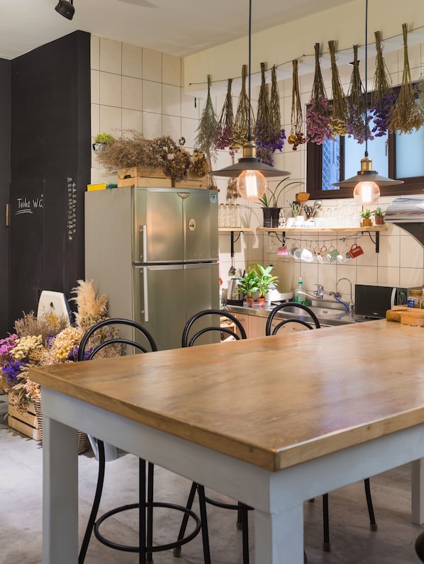 A modern kitchen with a wooden table, stainless steel appliances, hanging dried flowers, and a chalkboard menu.