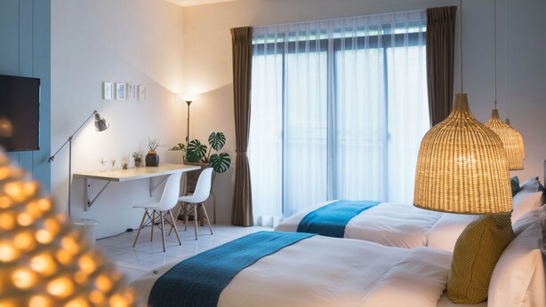 Una habitación de hotel con cama, escritorio, sillas, lámpara y un ventanal con cortinas.