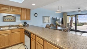 A kitchen with wooden cabinets, granite countertops, a dishwasher, and a dining area with wicker chairs and a table. - 112- Fabulous BEACH FRONT condo. Destin Beach Club (Destin)