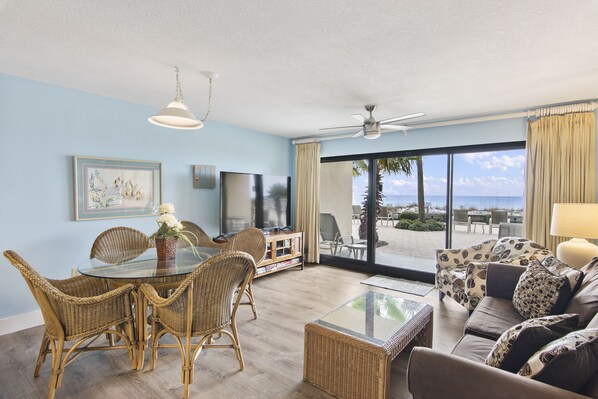 A spacious living area with a glass table, wicker chairs, a sofa, and a television.