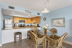 A kitchen with wooden cabinets, a stainless steel refrigerator, a microwave, and a dining area with wicker chairs and a glass table.