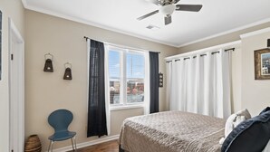 Un dormitorio con cama, una silla, ventana con cortinas, ventilador de techo y vistas al exterior.