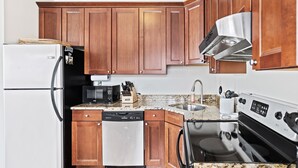 Una cocina con armarios de madera, campana extractora de acero inoxidable, lavavajillas, microondas y encimera de granito.