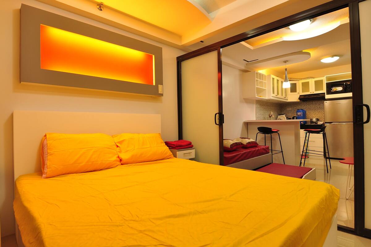 A room with a bed, a desk, and a kitchenette.