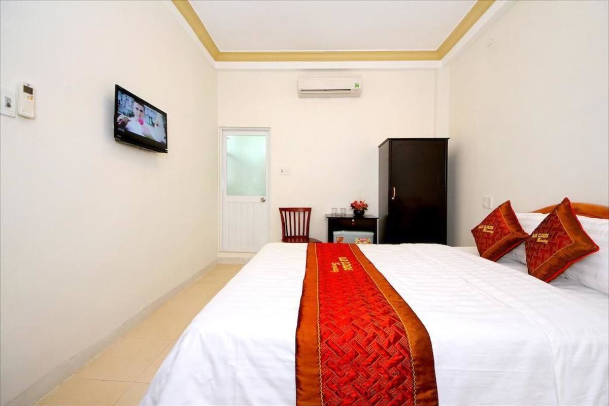 A hotel room with a large bed, a television on the wall, a wardrobe, and a small table with a vase.