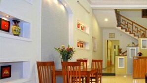 A dining area with a wooden table and chairs, a vase of flowers, and wall-mounted shelves with decorative items. - Blue Clouds Homestay (Da Nang)