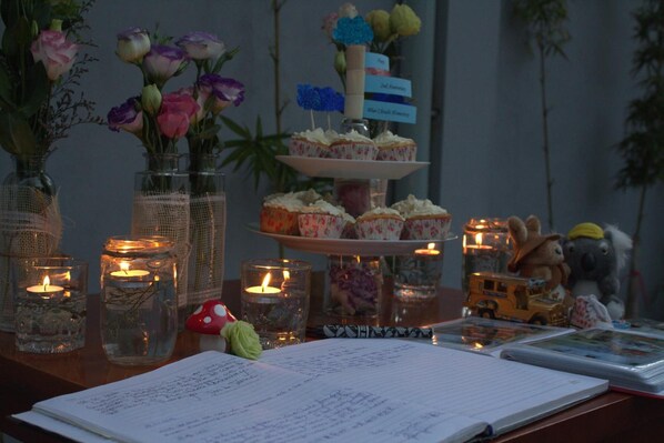 A table with a notebook, candles, a tiered cupcake stand, and decorative items. - Blue Clouds Homestay (Da Nang)