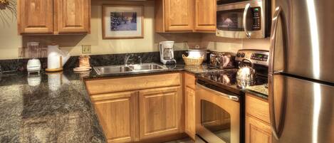 A kitchen with wooden cabinets, stainless steel appliances, a granite countertop, and a tiled backsplash.