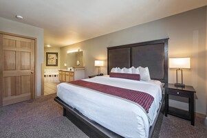 A hotel room with a large bed, two bedside tables, a wooden door, a bathroom with a tub, and a mirror.