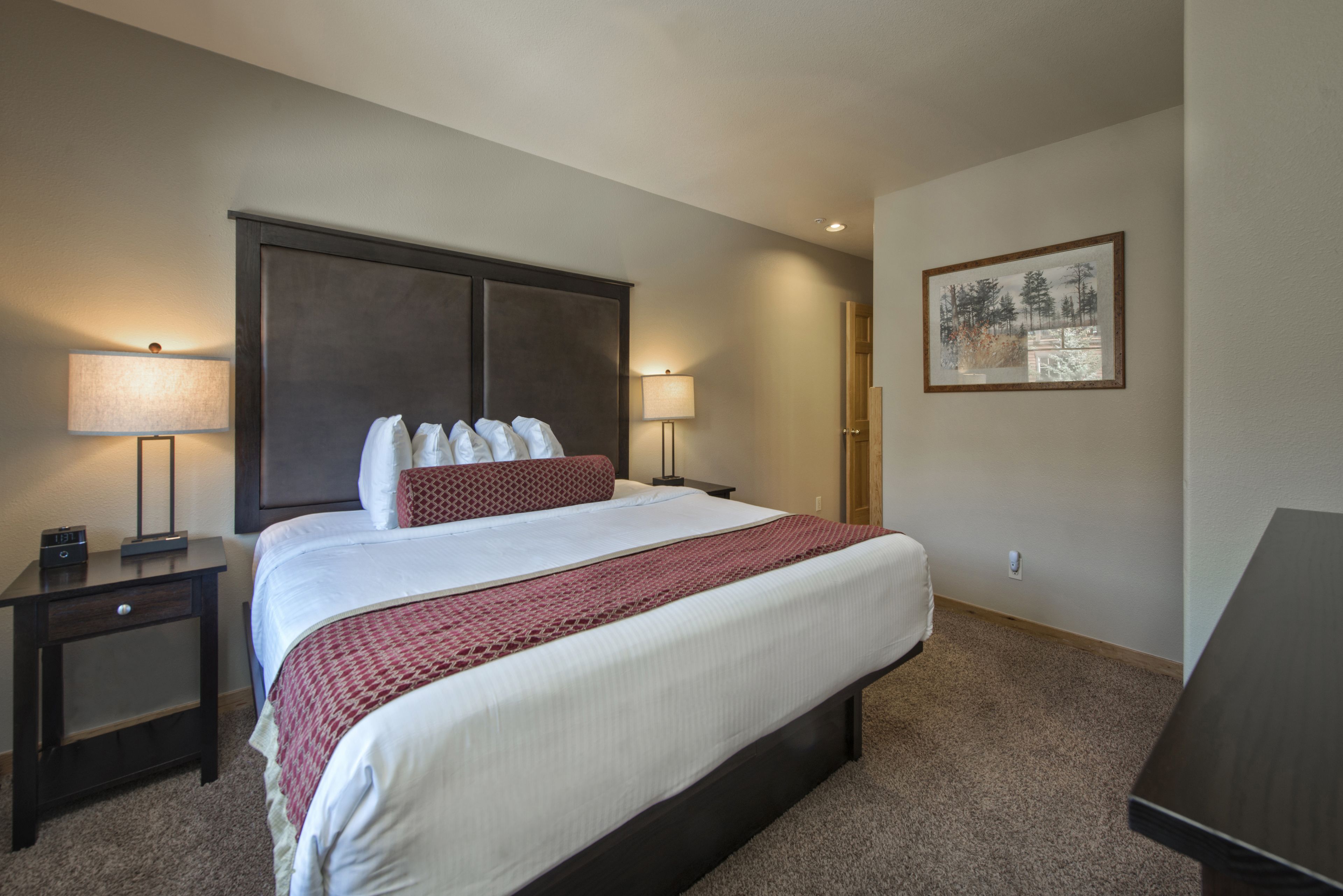 A hotel room with a large bed, two bedside tables, a nightstand, a lamp, and a framed picture on the wall.