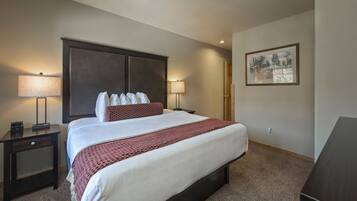 A hotel room with a large bed, two bedside tables, a nightstand, a lamp, and a framed picture on the wall.