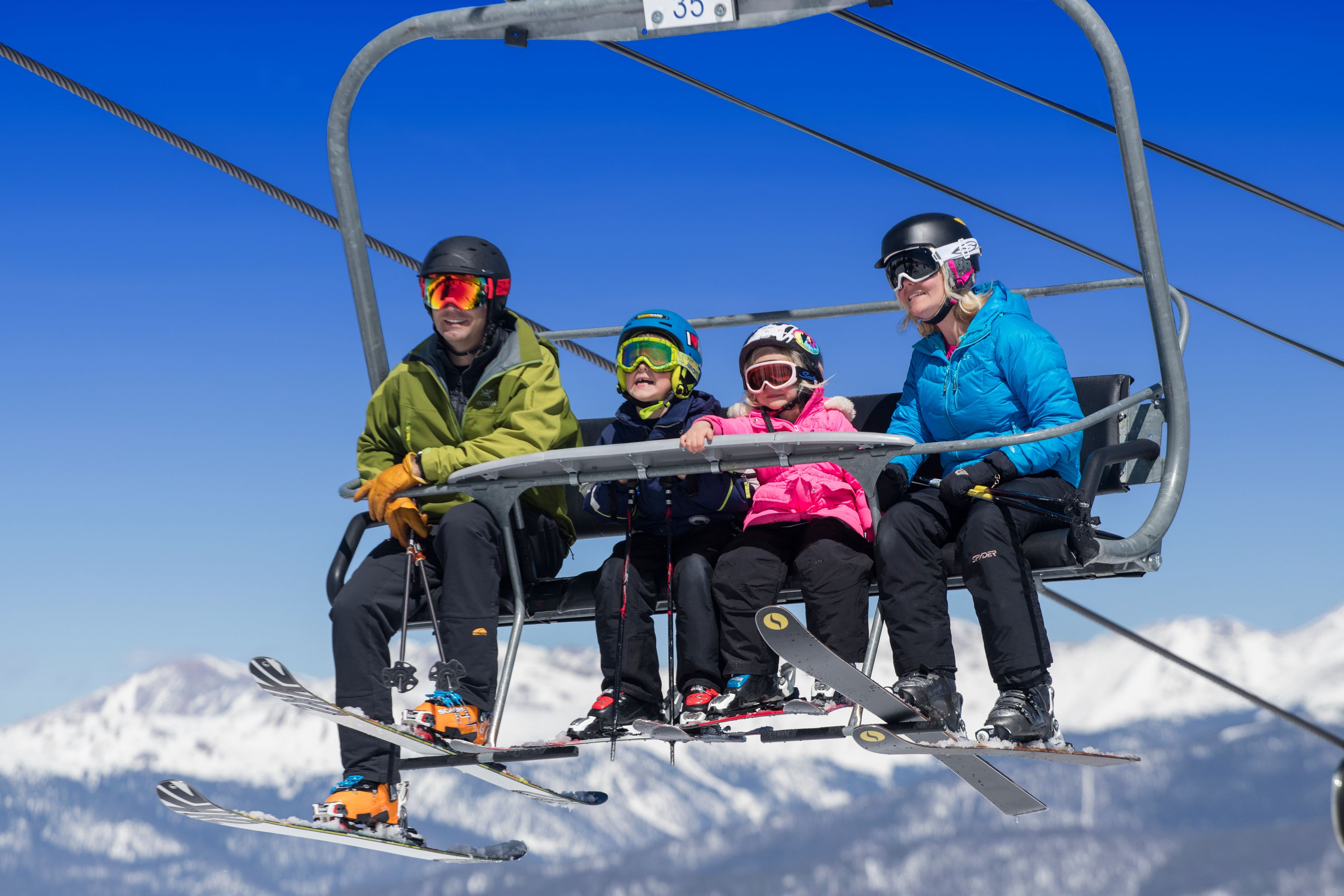 Un groupe de personnes se trouve dans un télésiège, avec des montagnes enneigées en arrière-plan.