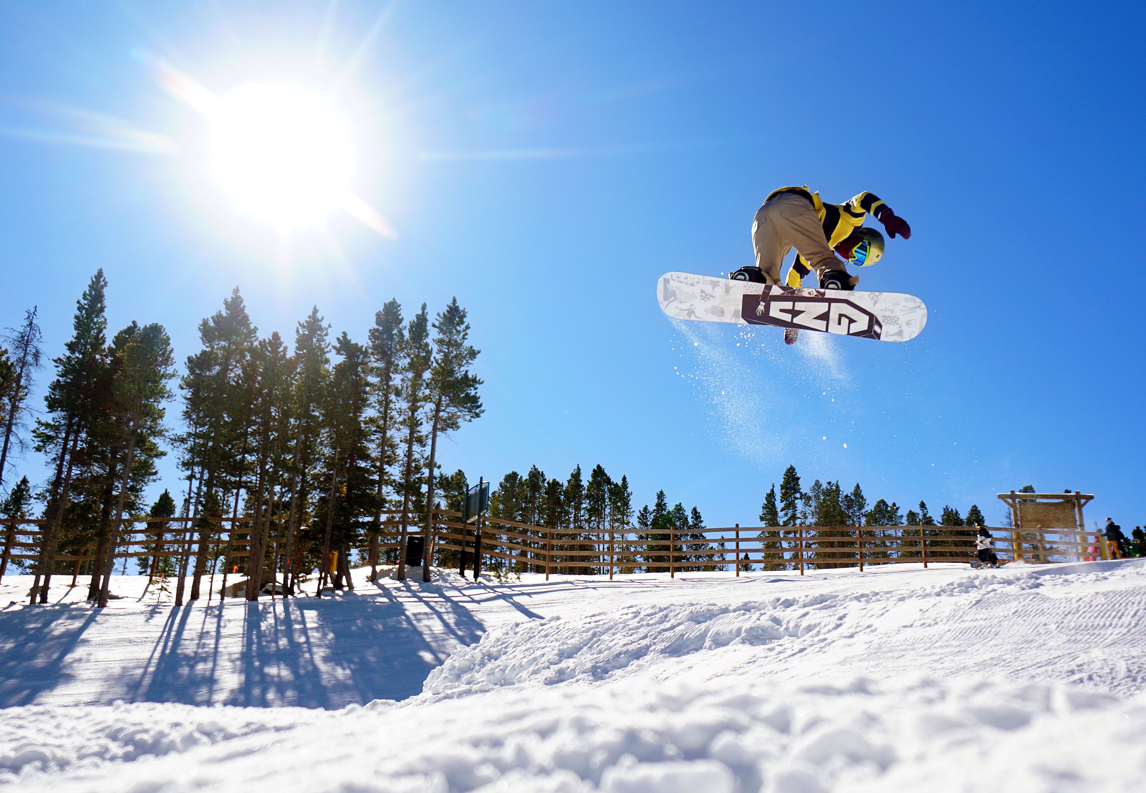 A snowboarder performing a jump with a clear sky and trees in the background.